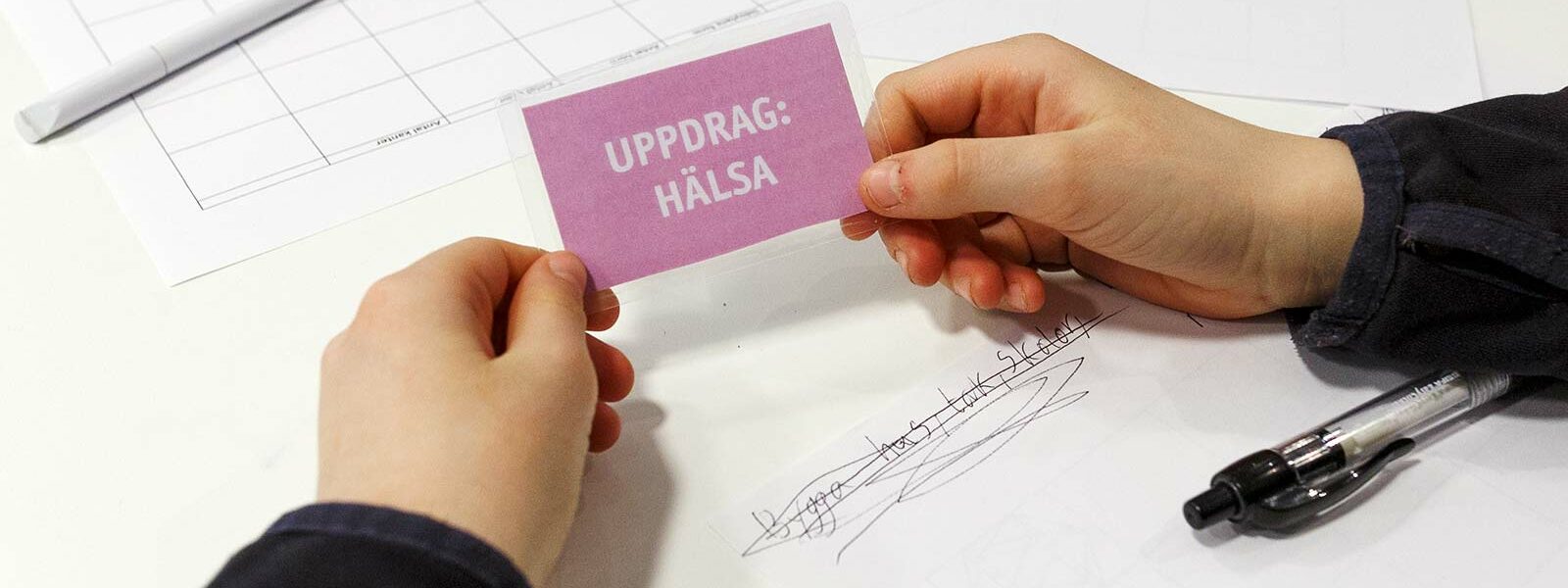 Två händer som håller en liten rosa skylt med texten uppdrag hälsa