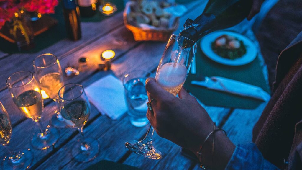 person som häller i champagne i sitt glas utomhus.