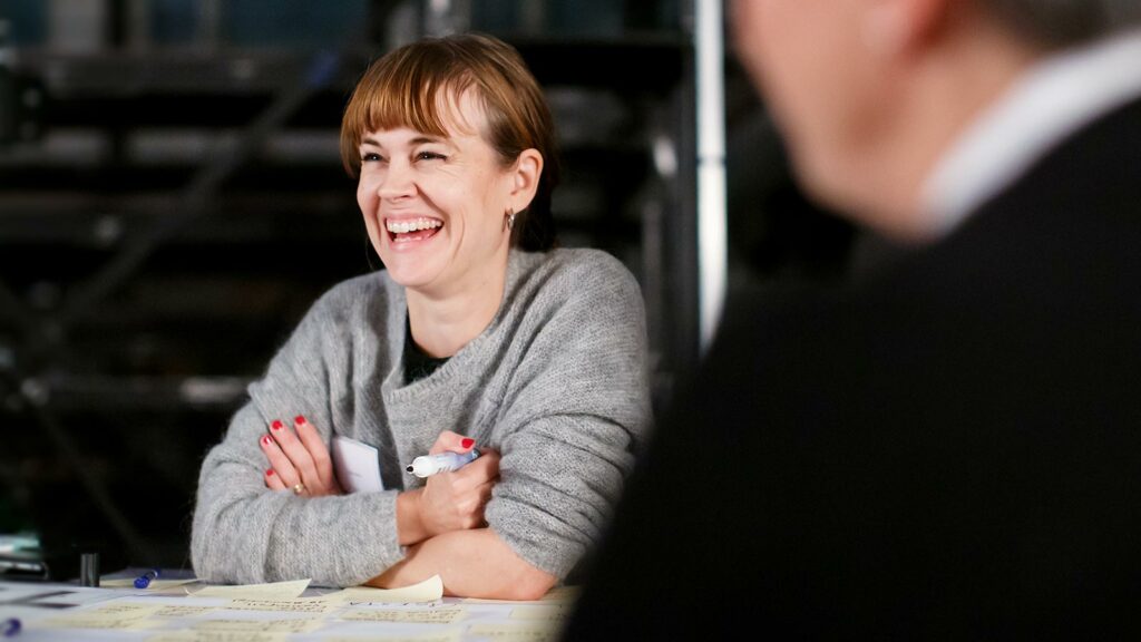 kvinna i workshop skrattar och ler brett medan hon håller i en penna